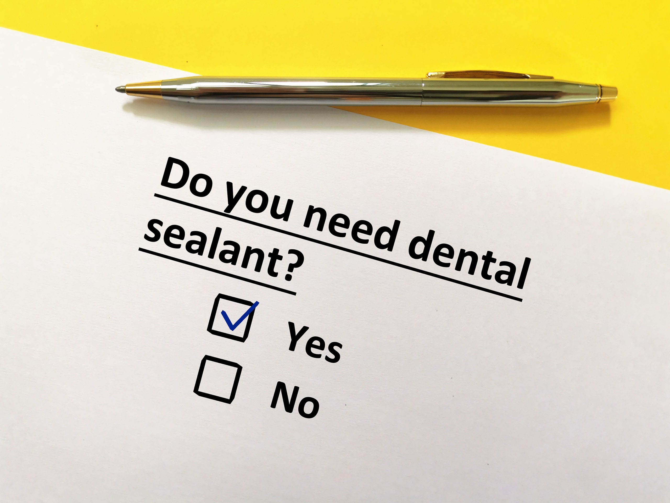 Printed sheet reading “Do you need dental sealant?” with Yes checked and No option below, a pen resting on a yellow and white background