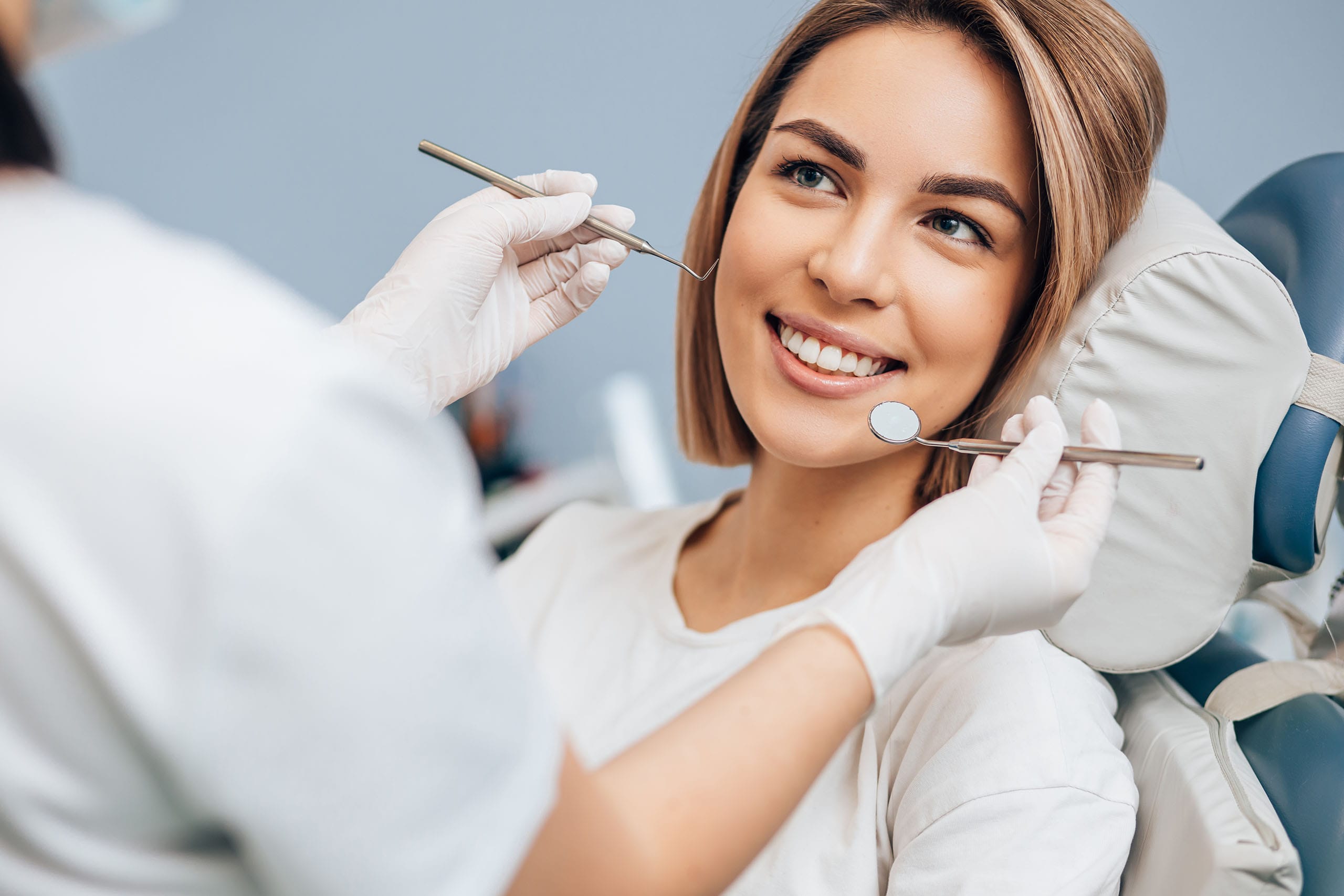 Dental hygienist examining a patient’s teeth with mirror and probe while the patient smiles in a dental chair
