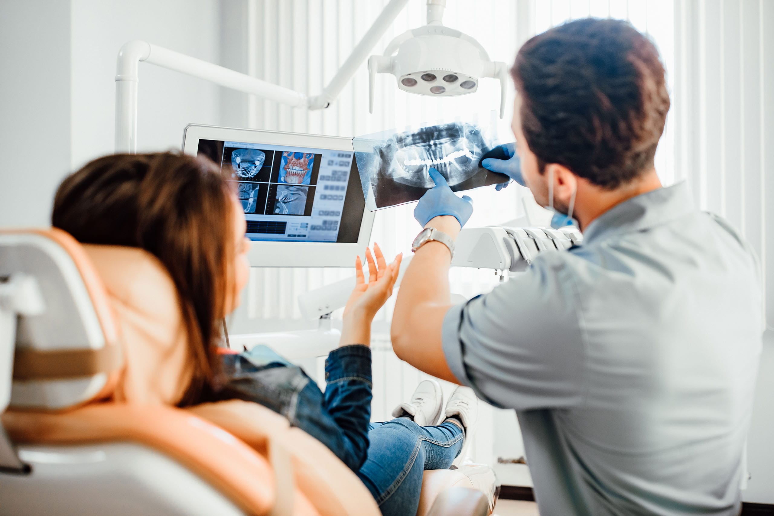 Dentist showing a patient a panoramic dental X-ray on a monitor and pointing out teeth during a consultation